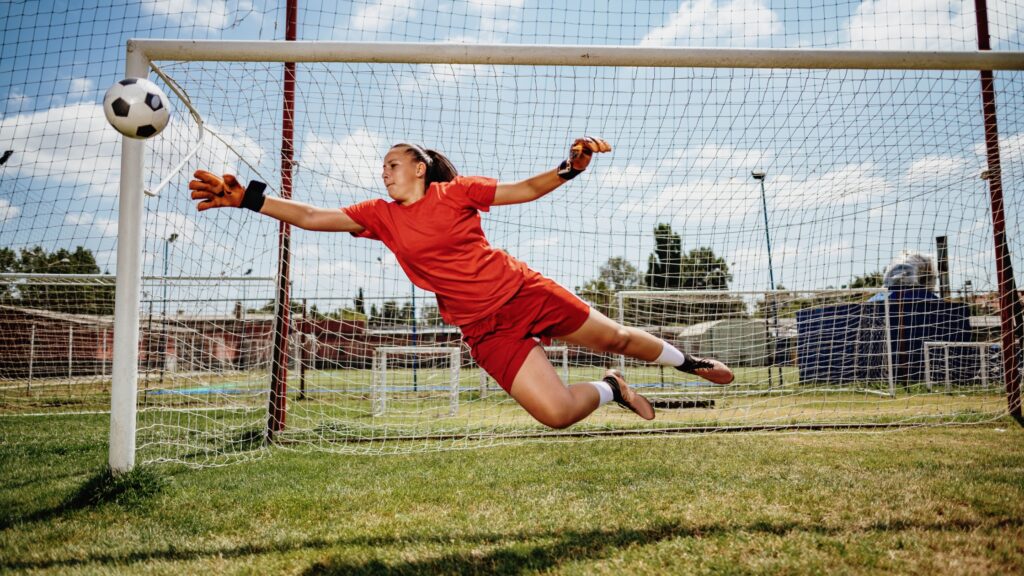 photo of girl blocking soccer ball in front of goalie net