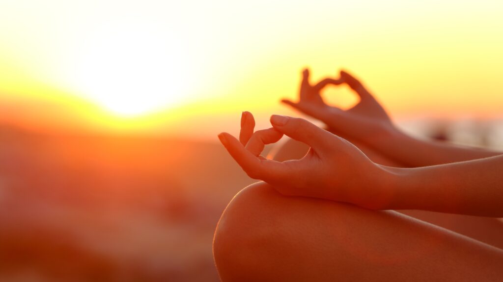 a woman meditating with her hands on her knees with the sunset in the background